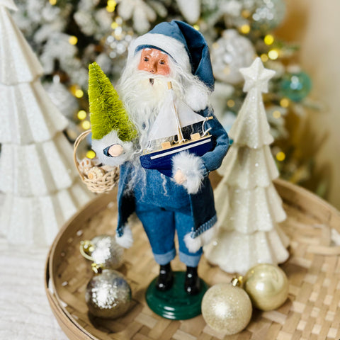 Decorative figure of a gnome holding a ship, surrounded by Christmas ornaments and trees.